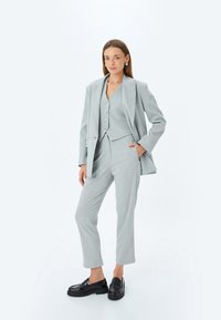 Grauer Blazer und passender Weste mit Knöpfen, maßgeschneiderte Hose und schwarze Loafers. Angenehmer Stoff mit subtiler Textur und nahtlosem Design.