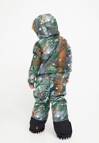 Farverigt polstret vinterdragt med et skovmønster og snefnug, herunder nuancer af grøn, brun og hvid. Inkluderer en hætte og sorte detaljer.