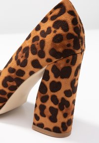 Lodička na vysokém podpatku s leopardím vzorem, zaobleným blokovým podpatkem a měkkým texturovaným materiálem v hnědých a černých tónech.