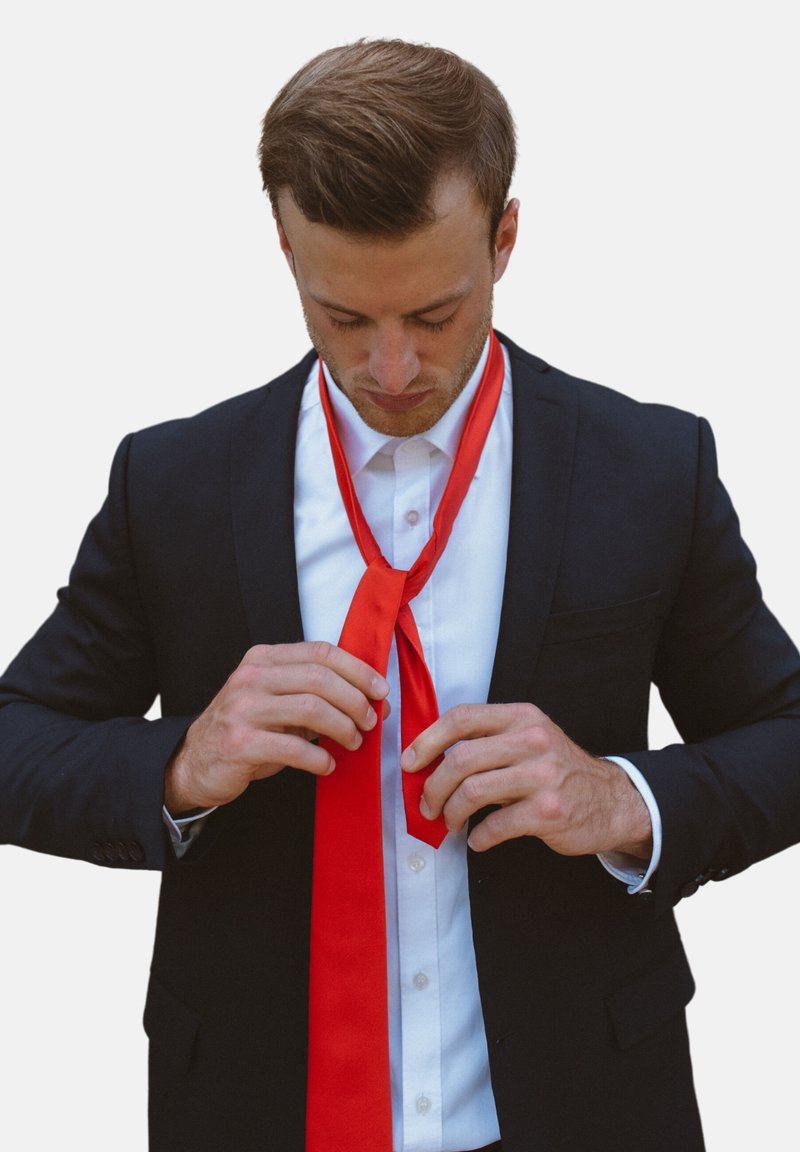 Corbata roja de seda siendo ajustada por una persona que lleva una chaqueta de traje negra y una camisa blanca, con una textura suave y un color vibrante.