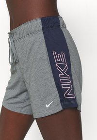 Pantalones cortos deportivos grises con un panel lateral azul marino que presenta un logo rosa de "NIKE", cinturilla elástica, cordón y un pequeño detalle de swoosh blanco.