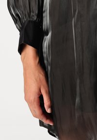 Bluză neagră din material translucent, cu mâneci lungi și bombate. Textură netedă, design elegant, având o bandă solidă neagră la încheietura mâinii.