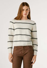 Witte, gestreepte trui van zachte wol met zwarte horizontale lijnen. Heeft een ronde halslijn en ribbels bij de manchetten, gecombineerd met een paarse corduroy broek.