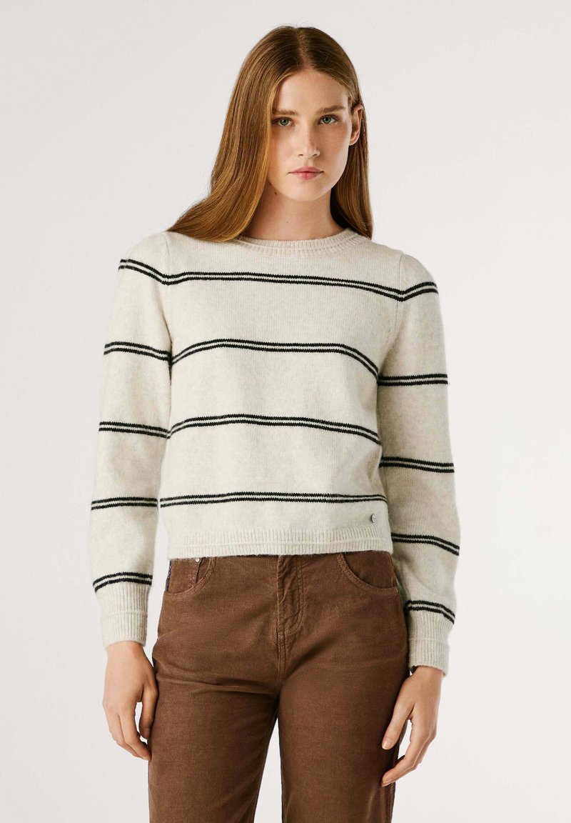 Witte, gestreepte trui van zachte wol met zwarte horizontale lijnen. Heeft een ronde halslijn en ribbels bij de manchetten, gecombineerd met een paarse corduroy broek.