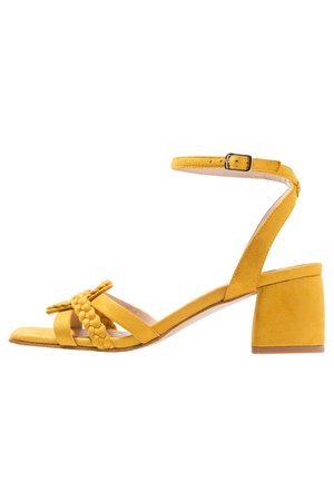 Gele suède sandaal met hak, voorzien van een gevlochten voorkant en een enkelbandje, met een blokhak en een gladde binnenzool.