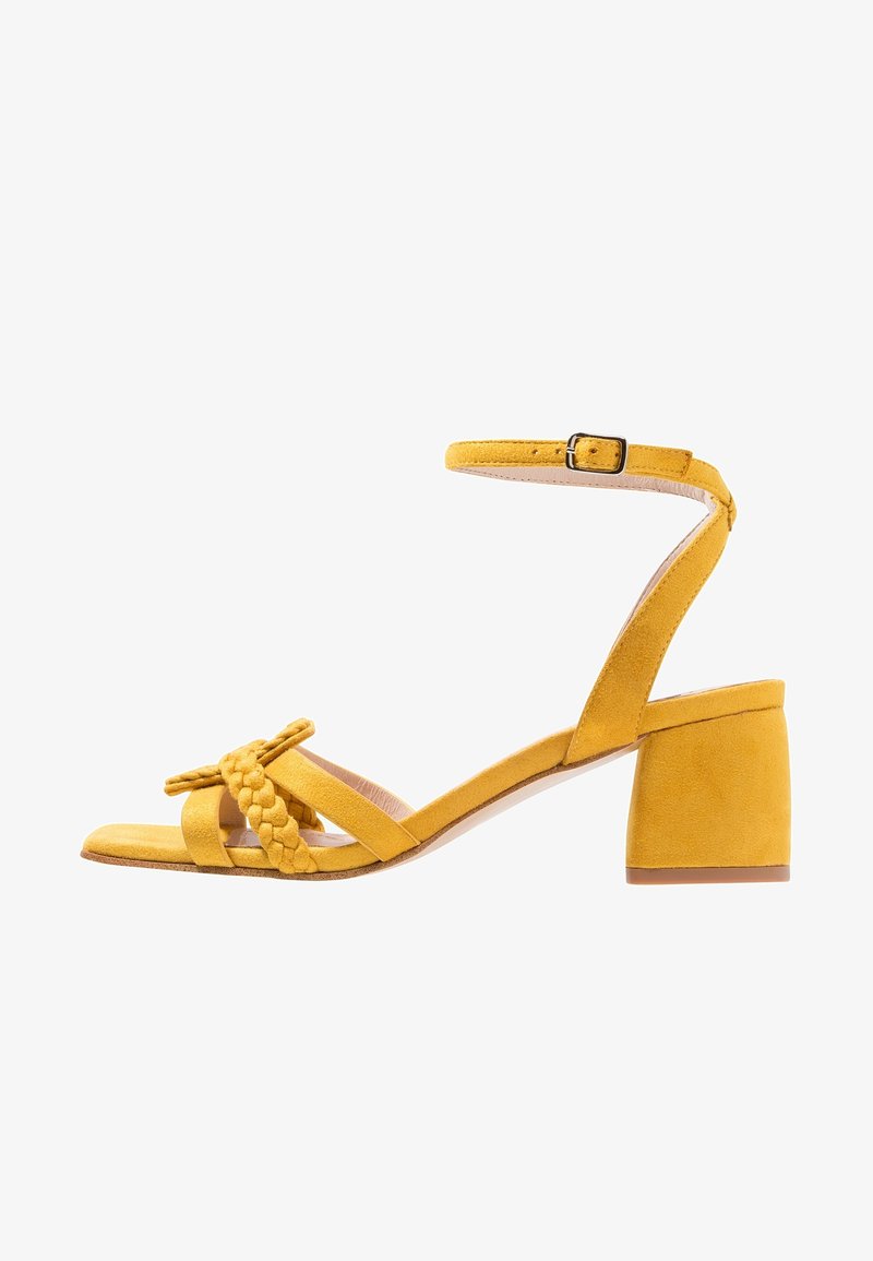 Sandale à talon en daim jaune avec un détail tressé à l'avant et une bride à la cheville, dotée d'un talon bloc et d'une semelle intérieure lisse.