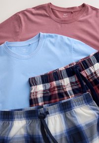 Deux t-shirts à col rond rose poudré et bleu clair associés à un short à cordon à carreaux rouges et bleus sur une surface plane.
