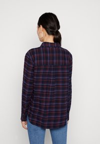 Camicia in flanella a quadri blu navy e bordeaux, con maniche lunghe, colletto e orlo arrotondato, mostrata da dietro.