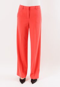 Pantaloni larghi corallo realizzati in un tessuto liscio, con frontale piatto e tasche laterali, abbinati a tacchi neri a punta.