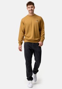 Sennepsgule sweatshirt med rund halsudskæring, ribbet manchetter og logo detaljer. Sammen med mørke jeans og hvide sneakers.