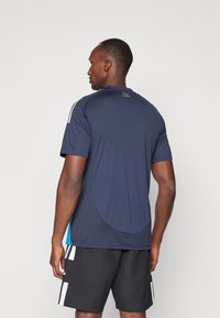 Camiseta atlética de la marina con mangas cortas, dobladillo curvado y acentos azules, hecha de un tejido transpirable. Presenta dos rayas blancas en los hombros.