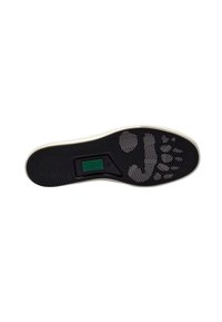 Suela de zapatilla de goma negra con un patrón de espiga, que presenta una etiqueta verde y un borde blanco contrastante que rodea la suela.