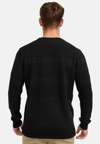 Maglione nero con strisce orizzontali testurizzate, scollatura a girocollo e maniche lunghe. Il materiale sembra leggero e leggermente elasticizzato.
