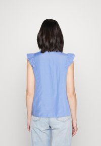Top senza maniche a righe blu con spalline arricciate, texture liscia e design aderente. Lo sfondo è bianco uniforme.
