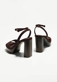Sandali con tacco alto in suede marrone, con un grosso tacco a blocco a righe, punta aperta e cinturino sottile alla caviglia. Piattaforma testurizzata per una maggiore altezza.