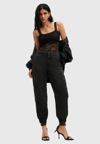 Zwarte kanten bodysuit met brede banden, gecombineerd met hoge zwarte cargo-broeken met taps toelopende boorden en zakken. Hak sandaaltjes maken de look compleet.