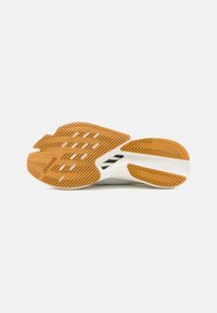 Schuhsohle mit einem strukturierten orangen Gummiunterteil, das Rillen und Ausschnitte für Grip aufweist, und einer eleganten weißen Zwischensohle.