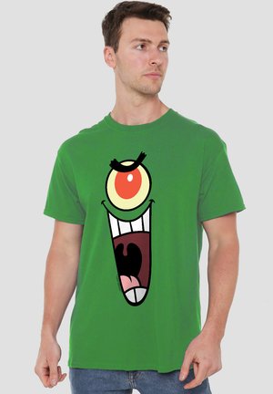 Grünes Baumwoll-T-Shirt mit einem großen Grafikmotiv eines Cartoon-Charakters, der ein übertrieben großes Gesicht mit Mund und Auge zeigt, wobei kräftige Farben und kontrastierende Details hervorgehoben werden.
