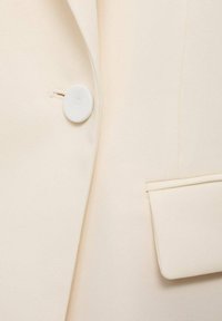 Lichtcrème blazer stof met een gladde textuur, voorzien van een ronde witte knoop en een zijzak voor een nette, op maat gemaakte uitstraling.