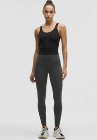 Top senza maniche nero abbinato a leggings grigi scuri a vita alta. La modella indossa scarpe da ginnastica bianche e nere. Tessuto liscio e aderente.