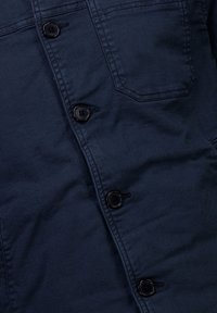 Takkimekko sinimustasta denimmateriaalia, jossa on napitusmustat napit, kirjailtua yksityiskohtaa ja rintatasku, jossa on terävä läppä.