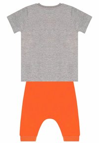 Szary T-shirt z krótkim rękawem i okrągłym dekoltem, w połączeniu z spodniami z elastycznym paskiem w kolorze pomarańczowym, charakteryzującymi się obniżonym krokiem.