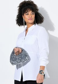 Weißes Langarmhemd mit Knopfverschluss, strukturiertem Stoff, zwei Brusttaschen, kombiniert mit einer glitzernden silbernen Clutch und einem silbernen Armband.