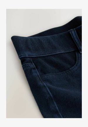 Tmavomodré džínsy zo silnej bavlny s plochým pásom, majú prednú vrecko, hladkú textúru a jemné švy.