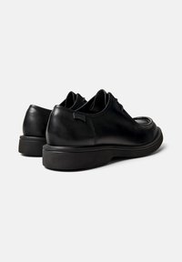 Schwarze Leder-Schnürschuhe mit dicken Sohlen, sichtbares Camper-Logo an der Seite, von hinten vor einem neutralen Hintergrund gezeigt.
