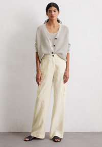 Light gray ribbed cardigan with black buttons, layered over a beige tank, paired with cream wide-leg linen trousers and black slide sandals.