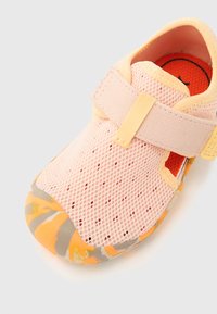 Ροζ δίχτυνο παπούτσι με λουράκι Velcro, με υφή από καουτσούκ σε κίτρινο και γκρι μαρμάρινο σχέδιο. Το εσωτερικό είναι έντονο πορτοκαλί.