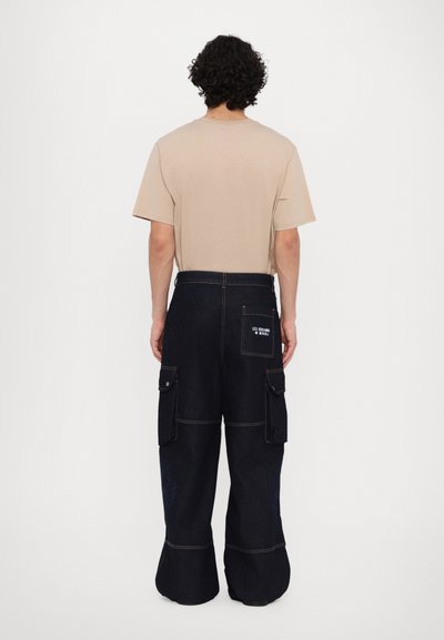 T-shirt en coton beige avec une coupe décontractée, associé à un pantalon cargo en denim foncé avec des poches et des coutures claires. Vue de dos.