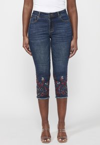 Dark denim capri jeans with floral embroidery in red and white at the hem, featuring a mid-rise waist and five-pocket design.