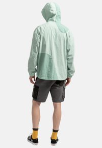 Lichtgroene hooded jacket met een gestructureerde afwerking en contrasterende kleurvlakken. Gepaarde met grijze cargoshorts met zakken.