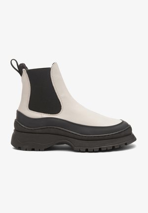 Botín Chelsea en beige y negro, con un durable upper de cuero, paneles laterales elásticos, suela gruesa negra y detalles texturizados.