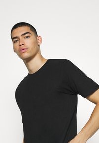 Černé tričko s krátkým rukávem a kulatým výstřihem, vyrobené z měkké bavlněné látky. Má slim fit a hladkou texturu.