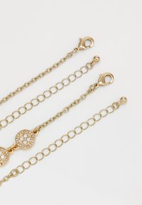 Three gold chain bracelets with lobster clasps, two featuring adjustable links, one adorned with round crystal-studded charms.