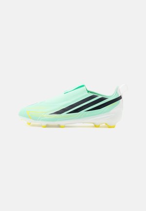 Chaussure de football vert clair avec des bandes diagonales noires, des accents jaunes et une semelle blanche avec des crampons jaunes, vue de profil sur fond blanc.