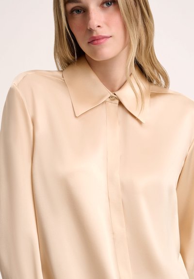 Beige silk blouse with a classic collar and front button closure. Smooth texture, long sleeves, and minimal stitching details.