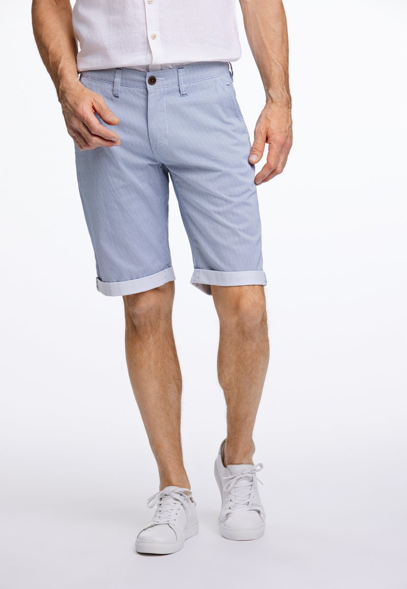 Pantaloni corti azzurri con una trama a motivo sottile, orli arrotolati e chiusura frontale con bottone. Abbinati a scarpe da ginnastica bianche.
