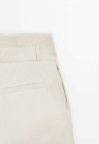 Beżowe spodnie wykonane z lekkiego materiału, z prostym przodem, boczną kieszenią i pojedynczą tylnią kieszenią z paskiem dekoracyjnym.