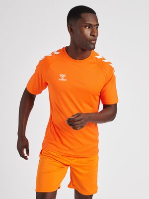Man in feloranje sportkleding aan het rennen, draagt een hummel-shirt met witte chevron-details op de schouders.