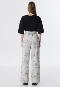 T-shirt noir oversize associé à un pantalon large gris clair avec des textes et des imprimés graphiques de style manuscrit. Tissu lisse, taille élastique.
