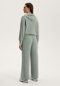 Ljust grön hoodie med en avslappnad passform, som har dragsko och ribbade muddar. Matchas med vida byxor i samma färg och vita sneakers.