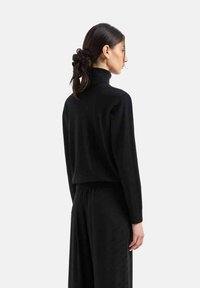 Maglione nero a collo alto con una vestibilità morbida, texture a costine e maniche lunghe, abbinato a pantaloni neri a gamba ampia coordinati.