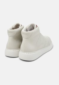Zapatillas de alta caña en cuero gris claro, con una textura suave, suelas de goma blancas y un diseño minimalista con un sutil logo.