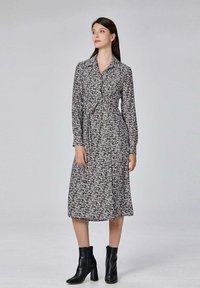 Robe florale noir et blanc à manches longues avec un col, froncée à la taille, accompagnée de bottines noires à la cheville. Texture mate, design mi-long.