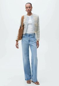 Giacca leggermente strutturata e multicolore con dettagli dorati, T-shirt bianco, jeans a gamba larga di un blu chiaro e borsa a tracolla marrone. Sfondo neutro.