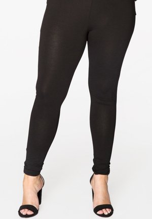 Leggings noirs en tissu extensible, avec un design élégant et une coupe fuselée, assortis à des sandales noires à talons hauts.