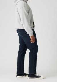 Huppari harmaana huppari, siniset farkut ja mustat lenkkarit. Farkut ovat klassista mallia, tummassa pesussa ja näkyvillä ompeluyksityiskohdilla.